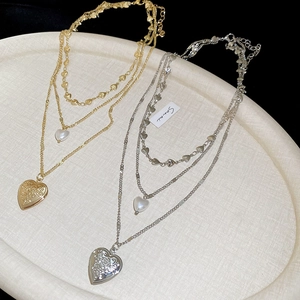 Detail of three-layer necklace featuring heart pendant, pearl, and rose relief accents