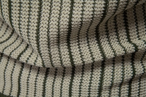 Close-up of beige knit fabric with vertical dark green stripes showing soft texture