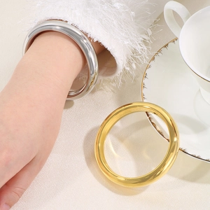 Polished minimalist 18k gold and silver stainless steel bangles shown on a textured background