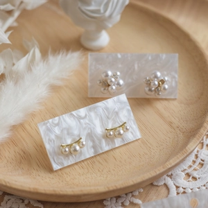 Elegant pearl and gold metal earrings set on marble card and wooden display tray