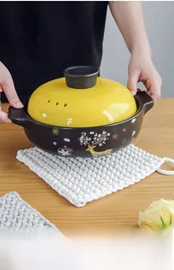 Detail of ceramic casserole on a woven cotton insulation mat with a wood table background