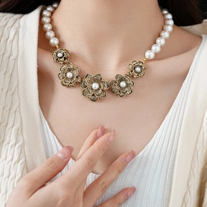 Detail of vintage necklace with white pearls and bronze flower pendants on a model