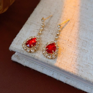 Close-up of gold earrings with red teardrop stones and sparkling diamond halo