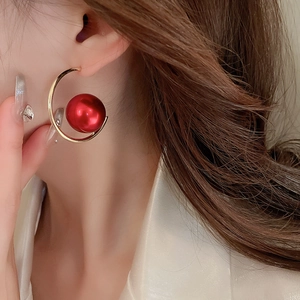 Close-up of a gold C-shaped earring with two large red beads worn on a model's ear