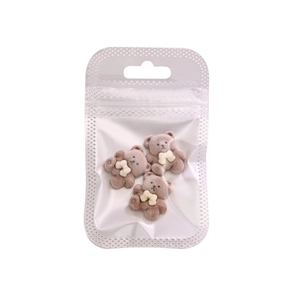 Three plush brown bear nail charms with white bows in a transparent hanging poly bag
