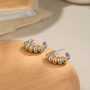 Detailed close-up of geometric twisted C-shape hoop earrings on a wooden display tray