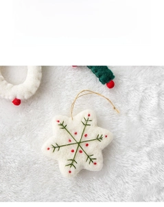 Macro detail of handmade white wool felt snowflake ornament with green and red embroidery