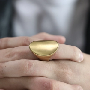 Macro shot of a wide oval stainless steel ring with a matte gold finish on model finger