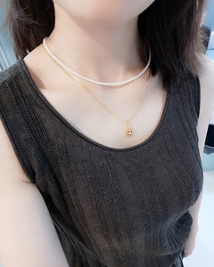 Close-up of layered pearl choker and gold chain necklace with square pendant on neck