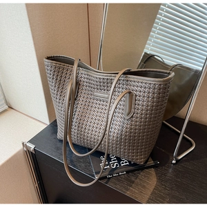 Detail of dark grey woven PU leather tote bag with long strap against minimalist backdrop