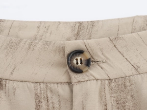 Dettaglio dei pantaloni beige stampati con girovita e bottone in resina marmorizzata