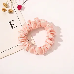 Close-up of a pink satin scrunchie with soft fabric pleats and elegant silk luster