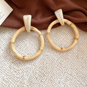 Detailed macro of bamboo hoop earrings with ivory marble resin studs on a textured display