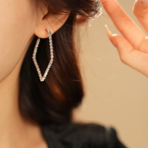 Macro view of a silver geometric twisted rhombus hoop earring worn on a model's ear