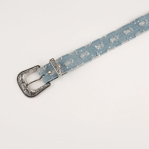 Detail of vintage carved metal buckle and distressed denim belt with silver sequins