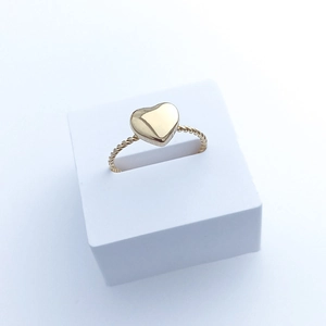 Macro detail of a golden heart ring with a twisted band displayed on a white stand