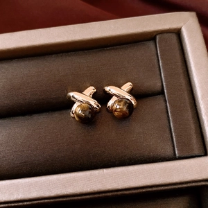 Close-up of 18k gold plated X-shaped stud earrings with tiger eye stone in a jewelry box