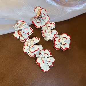Detail of tiered white floral drop earrings with red edges and golden hooks on silk cloth