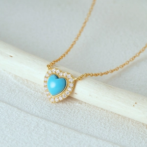 Macro shot of gold heart necklace with turquoise stone and zircons on a wooden prop