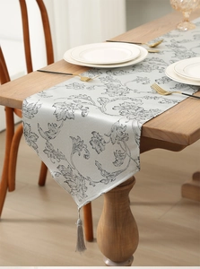 Close-up of silver-gray jacquard Christmas table runner with elegant tassels and tableware