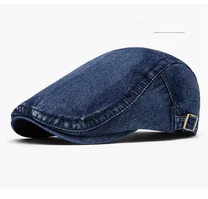 Detail of dark blue denim flat cap featuring adjustable metal side buckles and contrast stitching