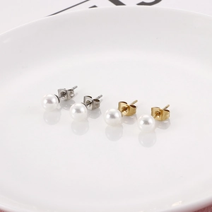 Elegant gold and silver round pearl stud earrings displayed on a white ceramic plate