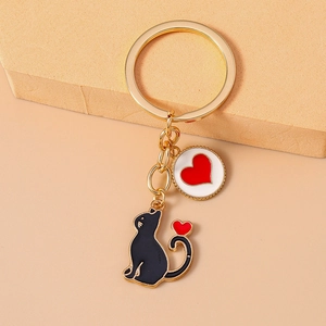 Detail of golden keychain with black enamel cat and white heart charm on beige background