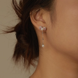 Close-up of dangling bow earrings with pink zircon and white pearls on model