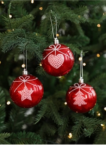 Detail of red Christmas baubles with heart and star patterns hanging on a tree