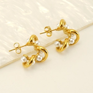 Detail of gold-plated C-shape twisted earrings featuring white pearls with a 18K finish