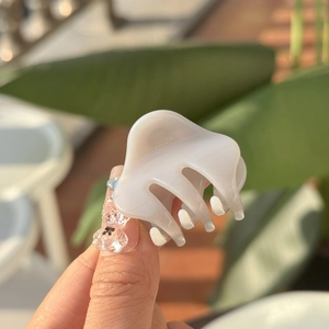 Detail showing creamy white mini hair claw clip held in hand for size visualization