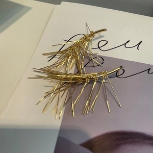 Dettaglio macro di orecchini dorati a forma di ago di pino su una rivista di moda