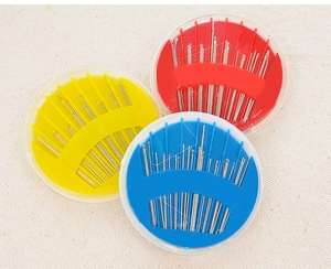 Close-up of three circular sewing needle cases in red, yellow, and blue on textured fabric