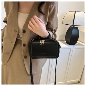 Detail of a black mini suitcase bag with dual gold zippers and pebbled texture leather