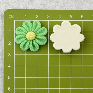 Close-up of 3cm resin flowers in green and cream showing size on a centimeter scale mat