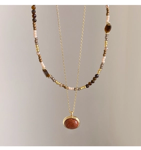 Close-up of layered necklace with tiger eye beads and shimmering goldstone pendant