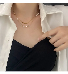 Detail of double-layer titanium steel necklace with gold chain and small white pearls on neck