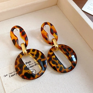 Macro view of geometric tortoiseshell acrylic hoop earrings on a textured jewelry tray