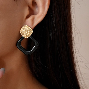 Close-up of geometric earrings with gold hammered texture and black square resin rings