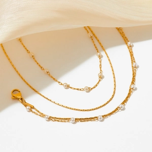 Detail of layered gold chain necklace featuring small white pearls and lobster clasp