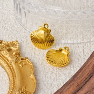 Two golden stainless steel seashell charms on a beige background for DIY jewelry making