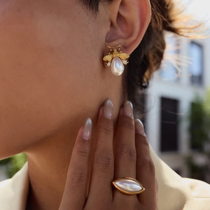 Elegant gold bee pearl earrings and oval shell ring worn in natural light setting