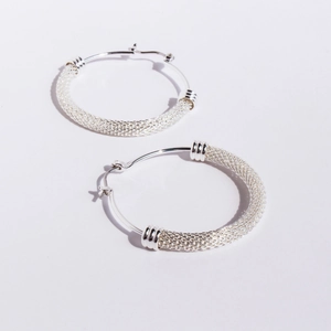 Silver woven mesh hoop earrings with decorative metal rings on a white background