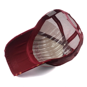 Detail view of burgundy mesh trucker hat lining with material labels and adjustable strap