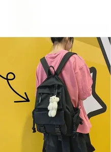 Detail of black canvas backpack featuring a plush bear pendant and side rope drawstrings