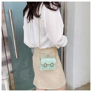 Detail of mint green PU leather satchel with gold chain on model against modern wall