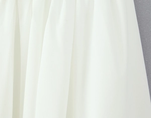 Close-up of white chiffon fabric showing soft texture and vertical drape of the dress