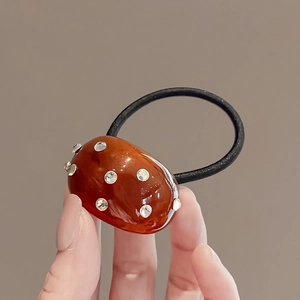 Détail d'une perle ambrée ovale avec strass fixée sur un élastique à cheveux noir