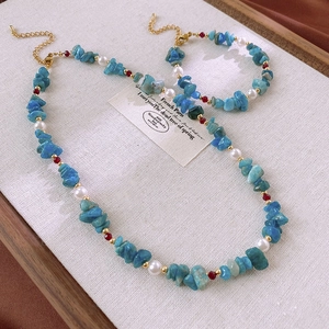 Close-up of aquamarine beaded necklace and pearl bracelet with golden clasp on white board