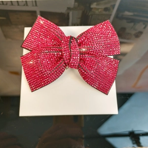 Close-up of a large red rhinestone bow hair clip on a white box with reflective background
